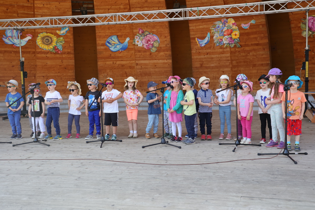 Grupa dzieci śpiewa na scenie. Wszystkie mają kapelusiki.