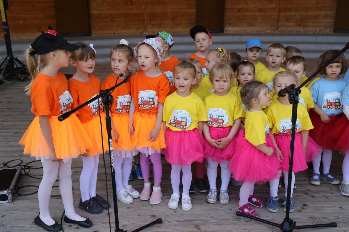 Przedszkolaki w kolorowych ubraniach śpiewają na scenie.