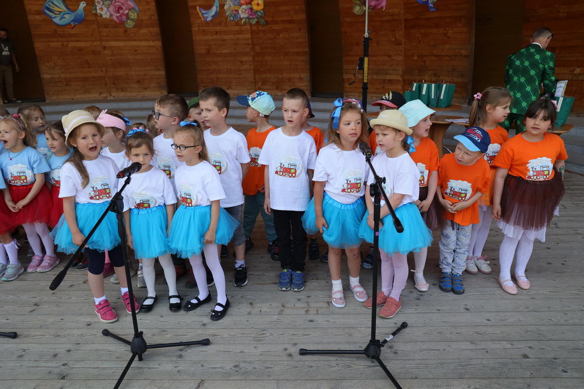 Przedszkolaki w kolorowych ubraniach śpiewają na scenie.