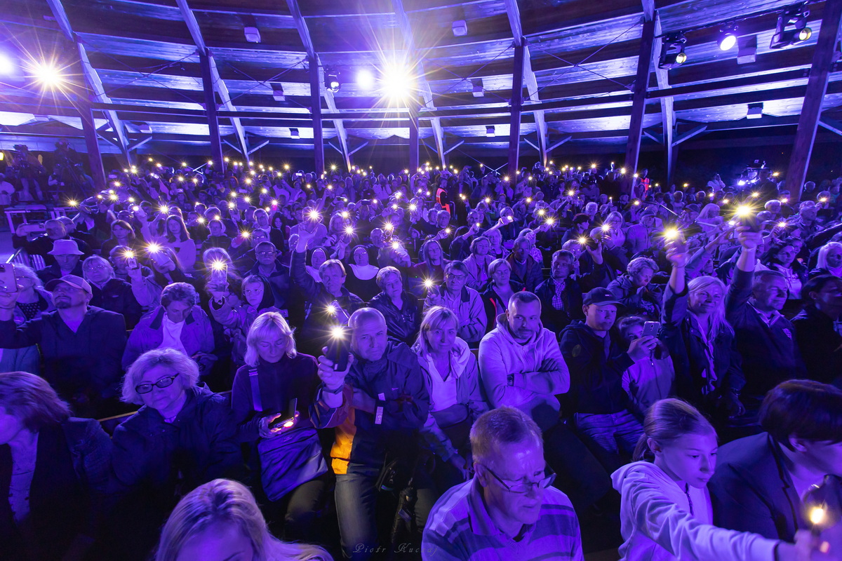 Publiczność w niebieskim świetle, niektórzy  trzymają świecące telefony.