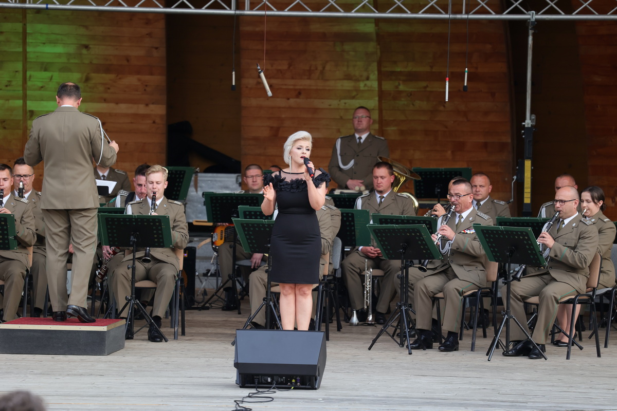 Artystka w czarnej sukni śpiewa na scenie.