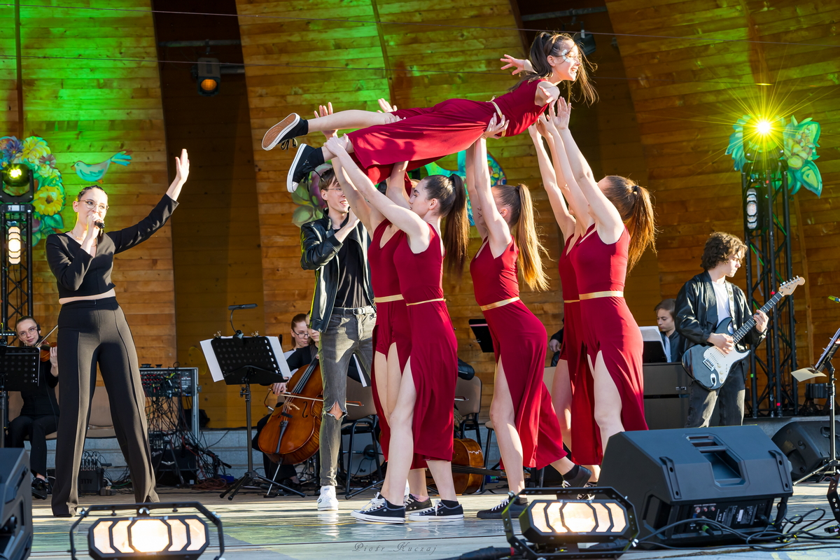 Cztery tancerki w czerwonych kostiumach unoszą piątą dziewczynę ponad głowami na rękach.