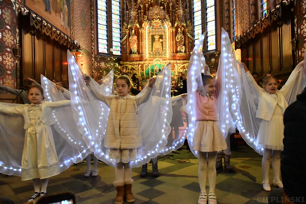 Dziewczynki ubrane na biało z pelerynami uniesionymi aby przypominały skrzydła aniołów.