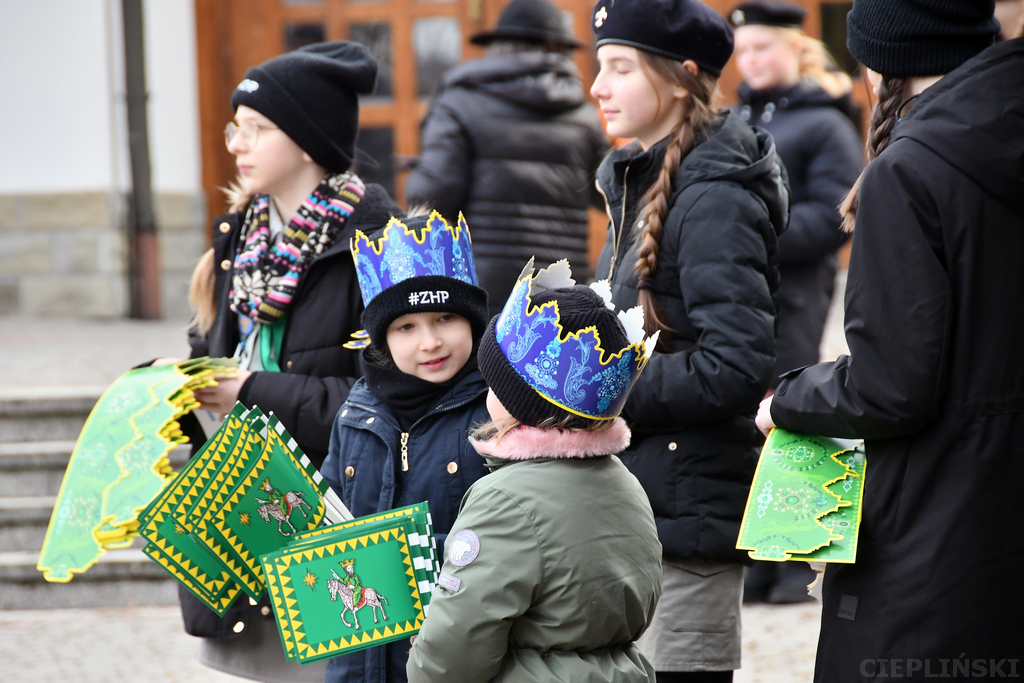Dzieci w czapkach z logo ZHP i koronach trzymają w rękach korony i chorągiewki dla uczestników.